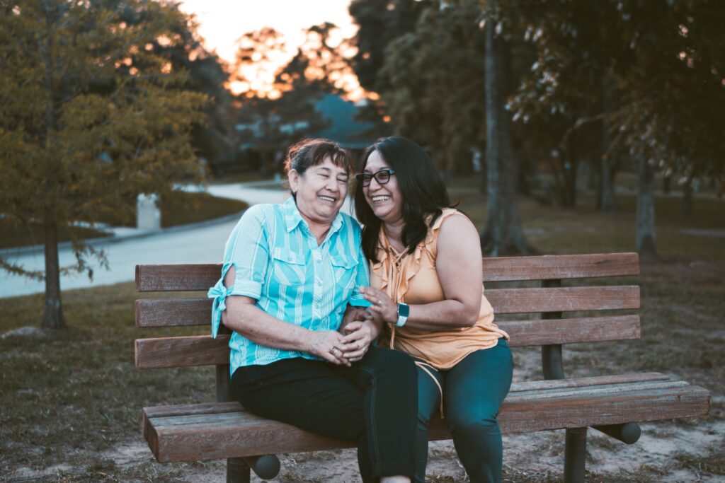 Two women siting on bench laughing.